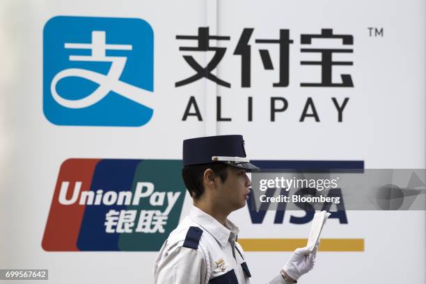 Security guard walks past signage for Ant Financial Services Group's Alipay payment system, an affiliate of Alibaba Group Holding Ltd., top, China...