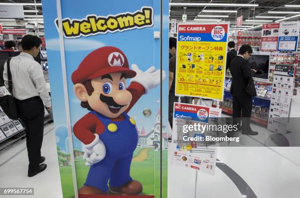 Customers are seen behind a poster of Nintendo Co.'s video-game character Mario displayed at the Bic Camera Akiba electronics store, operated by Bic...