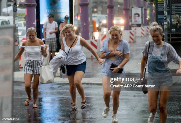 Tourists run to get out of the pouring rain on June 22, 2017 near the Checkpoint Charlie tourist attraction in Berlin. / AFP PHOTO / dpa / Kay...