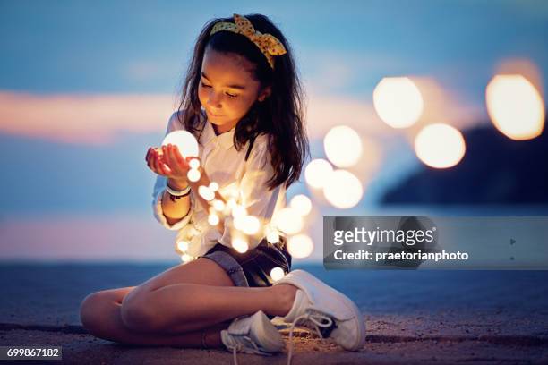 petite fille est assis sur la jetée et de jouer avec les lumières mystérieuses - pure photos et images de collection