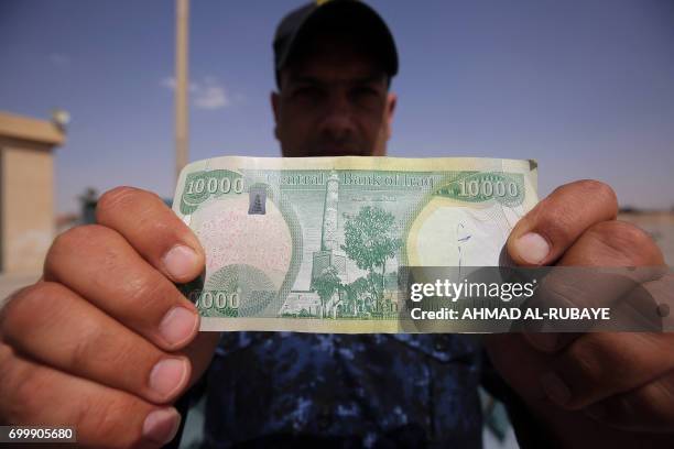 An Iraqi policeman displays a 10,000-Iraqi dinar banknote bearing an image of Mosul's iconic leaning minaret, known as the "Hadba" , on June 22 in...