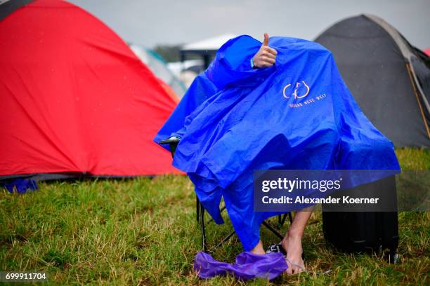 Festival goer hides under a rainjacket on the muddy camping compound ahead the Hurricane Festival 2017 on June 22, 2017 in Scheessel, Germany. The...