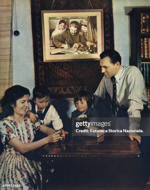 Stalin Personality Cult: photograph published on 'Union Soviétique - Mai 1953' . A typical Soviet family portrayed in their cozy apartment living...