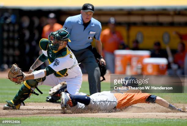 Josh Reddick of the Houston Astros scores sliding past Bruce Maxwell of the Oakland Athletics in the top of the first inning at Oakland Alameda...