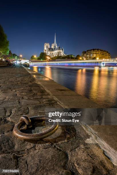 quayside of seine river with notre-dame cathedral and boat light trails on the water at sunset in paris, france. - quayside stock pictures, royalty-free photos & images