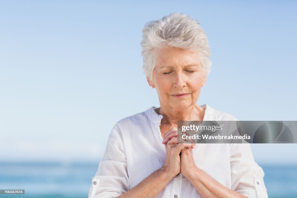 Senior woman praying on the beach