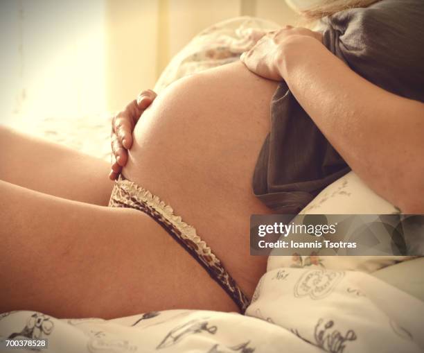 young pregnant woman lying on bed, hand on belly, close-up - tanga stock-fotos und bilder