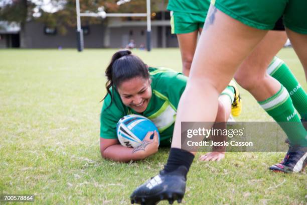 female rugby players in action, one player in sliding on ground with ball smiling - sportlerin stock-fotos und bilder