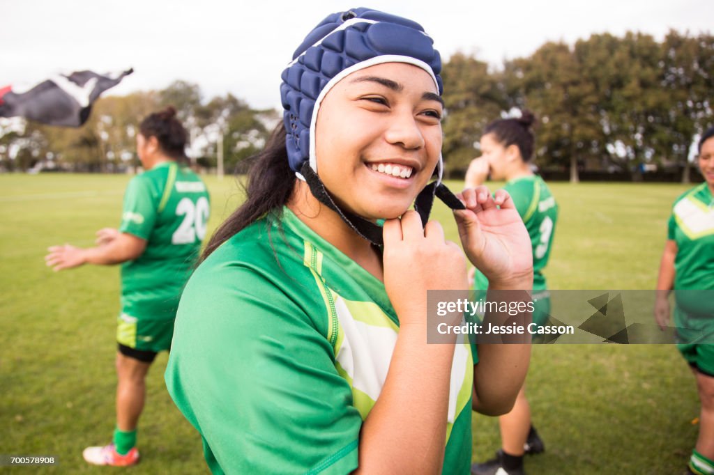 Female rugby player is smiling and putting on head gear