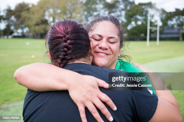 two female rugby players hugging on rugby field - rugby portraits stock-fotos und bilder