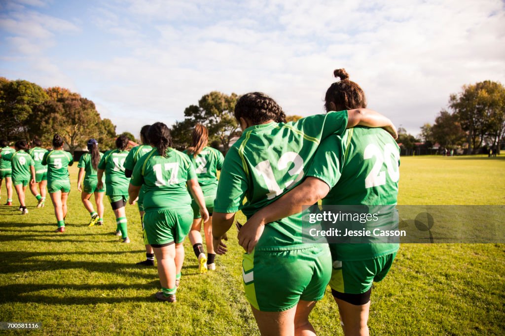 Line of female rugby players walking away from camera, one player is helping an injured player