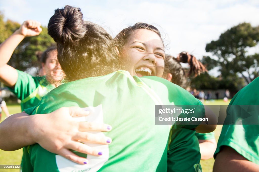 Two female sports players have celebratory embrace on field