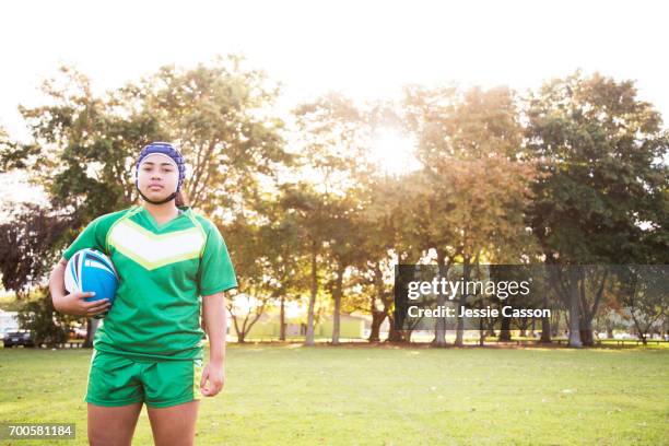 female rugby player stand holding ball on field, back lit with trees in background - grittywomantrend stock-fotos und bilder