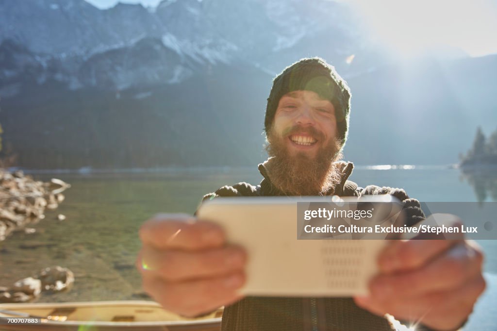 Young man standing beside lake, taking selfie, using smartphone, Garmisch-Partenkirchen, Bavaria, Germany