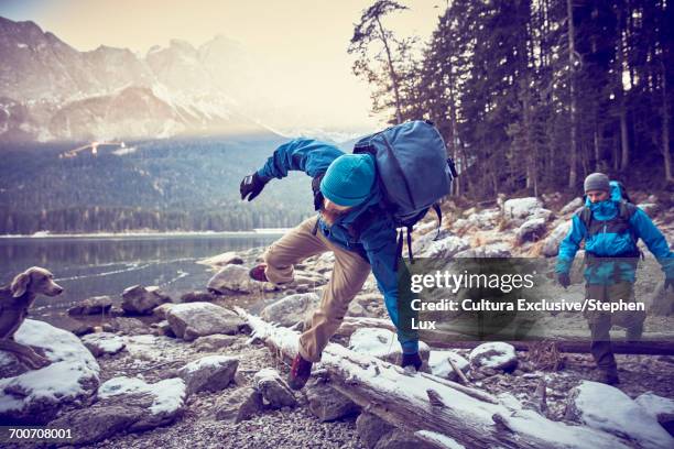 two male hikers jumping logs by snowy lake eibsee, zugspitze, bavaria, germany - alles hinter sich lassen stock-fotos und bilder