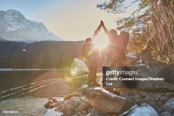 two male hikers high fiving by sunlit lake eibsee, zugspitze, bavaria, germany - celebrates exclusive sport cooperation stock pictures, royalty-free photos & images