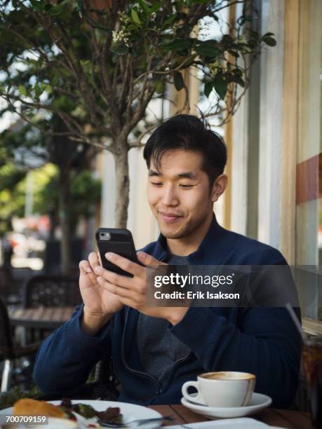 smiling chinese man texting on cell phone at outdoor cafe - man smile very casual relaxed authentic outdoor stock pictures, royalty-free photos & images