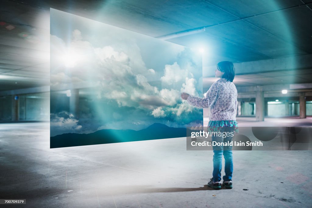 Mixed Race girl watching clouds on virtual screen in parking garage