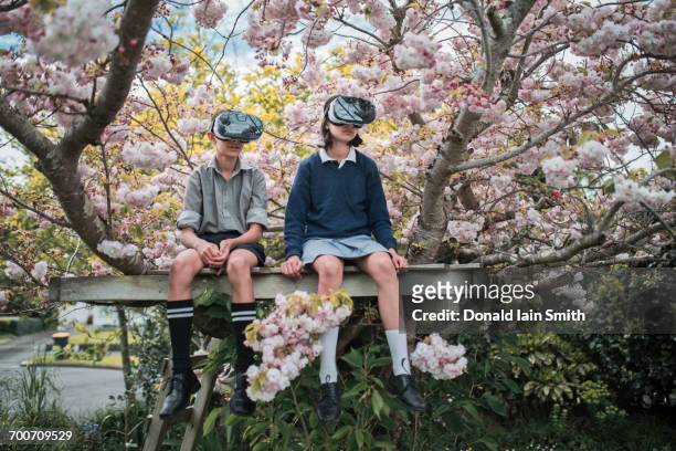 mixed race brother and sister sitting in tree wearing virtual reality goggles - mixed race brother and sister sitting in tree wearing virtual reality goggles stock-fotos und bilder
