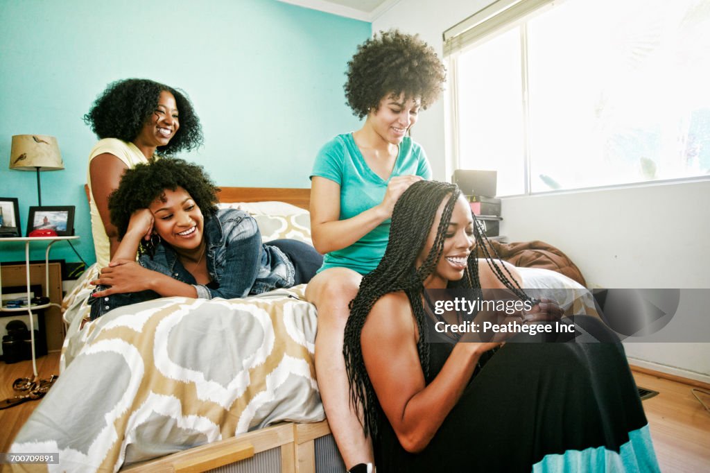 Woman braiding hair of friend in bedroom