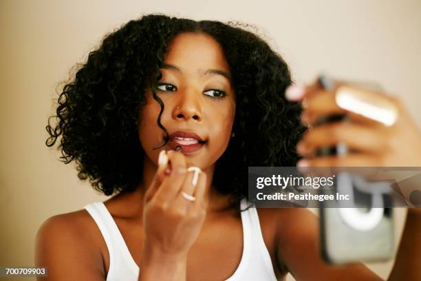 mixed race woman holding cell phone and applying lipstick - black makeup stockfoto's en -beelden