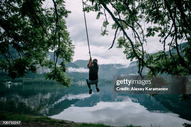 caucasian woman swinging on rope swing at lake - rope swing fotografías e imágenes de stock