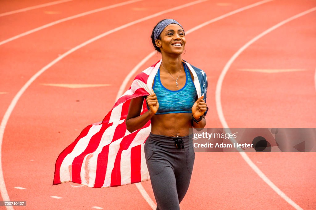 Smiling Black athlete holding American flag on track