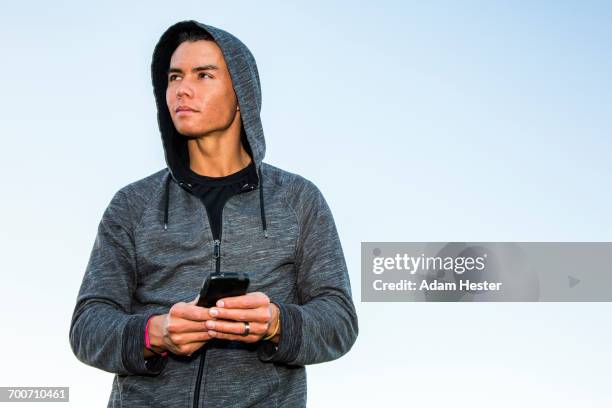 mixed race man wearing hoody texting on cell phone - mixed race man standing studio stockfoto's en -beelden
