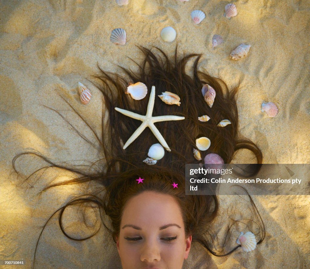 Pacific Islander woman laying on beach with seashells and starfish in hair