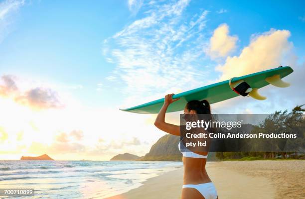 pacific islander woman standing on beach holding surfboard - mid adult women stock pictures, royalty-free photos & images