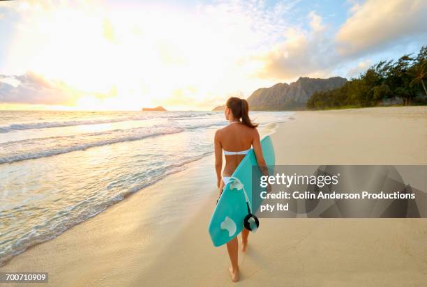 pacific islander woman walking on beach carrying surfboard - surfer stock pictures, royalty-free photos & images