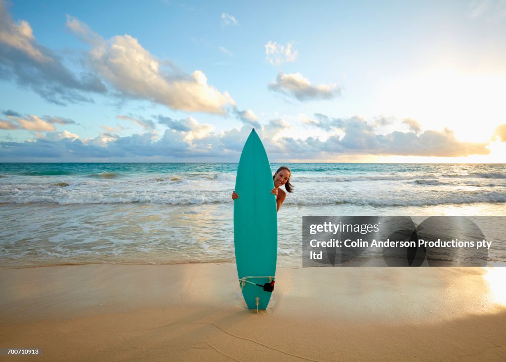 Pacific Islander woman standing on beach behind surfboard