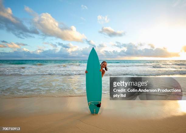 pacific islander woman standing on beach behind surfboard - beach hold surfboard stock-fotos und bilder