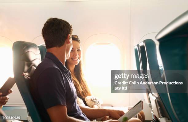 smiling couple sitting on airplane - couple airplane stock pictures, royalty-free photos & images