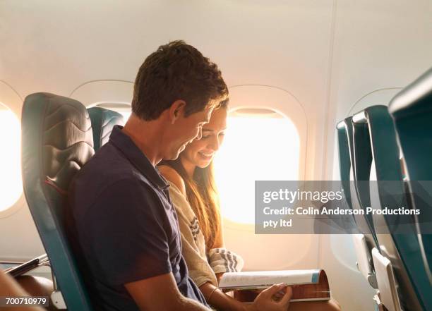 smiling couple reading magazine on airplane - couple airplane stockfoto's en -beelden