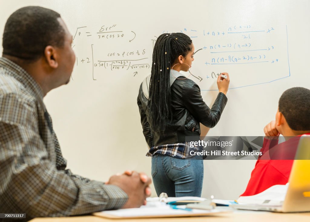 Teacher and student watching classmate writing equation on whiteboard