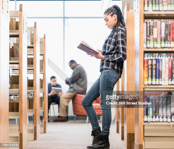 teenage girl leaning on library bookcase reading book - leaning stock pictures, royalty-free photos & images