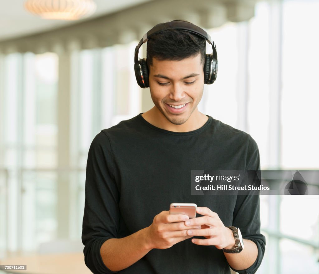 Hispanic man wearing headphones texting on cell phone