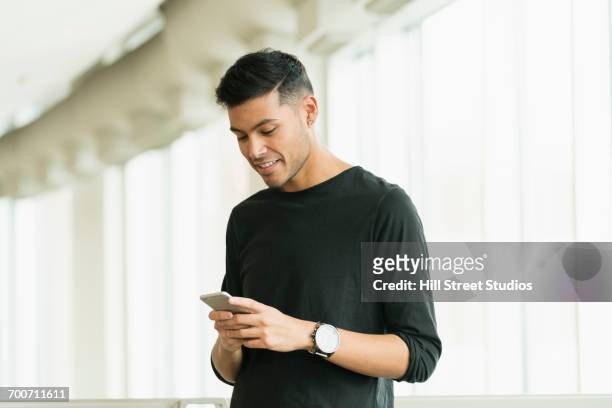 hispanic man texting on cell phone near window - call us photos et images de collection