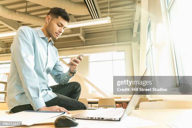 hispanic man sitting on table texting on cell phone - table low angle stock pictures, royalty-free photos & images