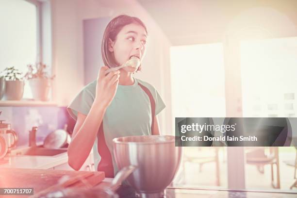 mixed race girl licking cookie dough on spoon - looking back stock-fotos und bilder