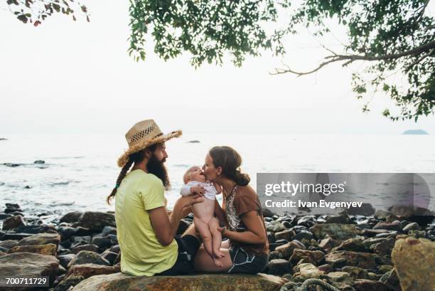 caucasian mother and father holding baby daughter on rocky beach - koh chang stock pictures, royalty-free photos & images