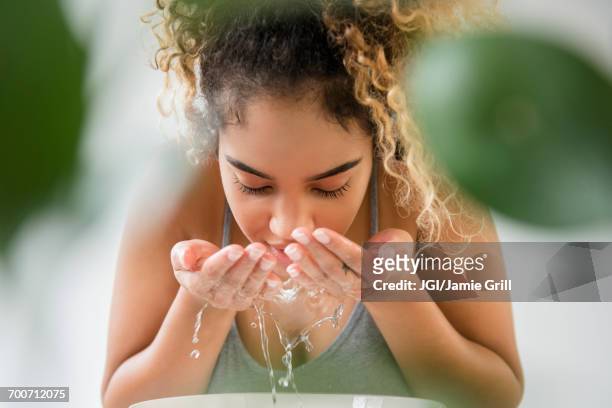 mixed race woman splashing water on face - routine foto e immagini stock