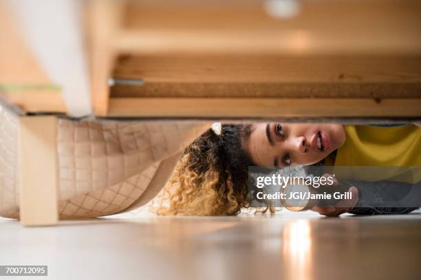 mixed race woman looking under bed with flashlight - angst stockfoto's en -beelden