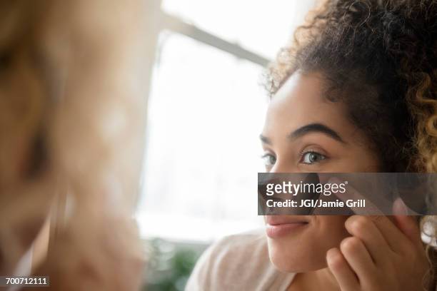 mixed race woman applying lotion to cheek - routine foto e immagini stock