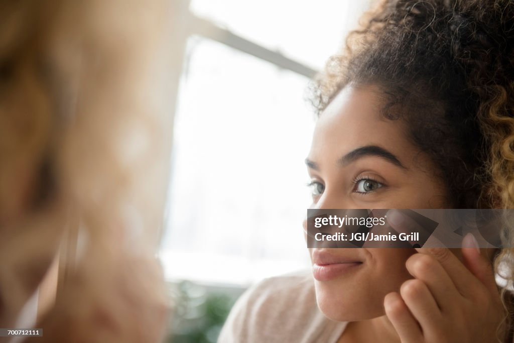 Mixed Race woman applying lotion to cheek