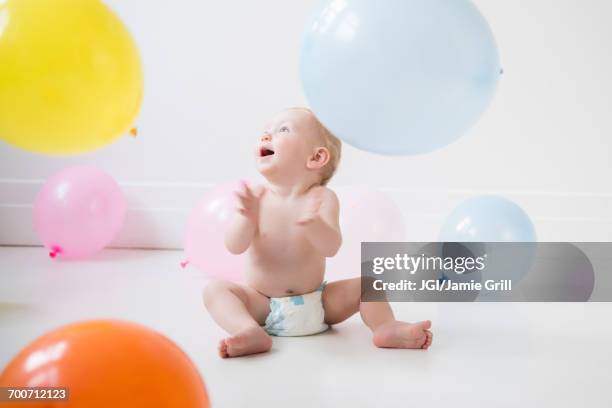 caucasian baby boy sitting on floor watching balloons - grill party stockfoto's en -beelden