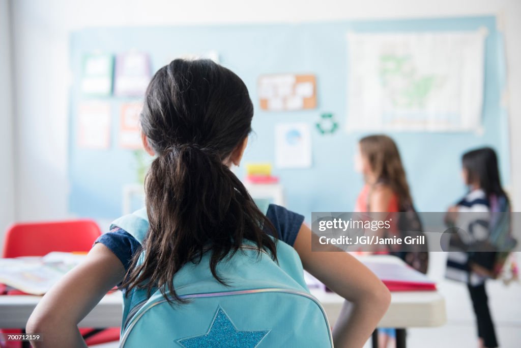 Girl in classroom wearing backpack watching classmates