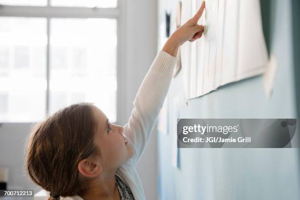 caucasian girl pointing to paper on wall - girl pointing stock-fotos und bilder