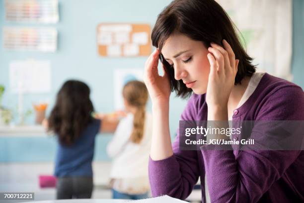 caucasian teacher with headache in classroom - overworked teacher stock pictures, royalty-free photos & images